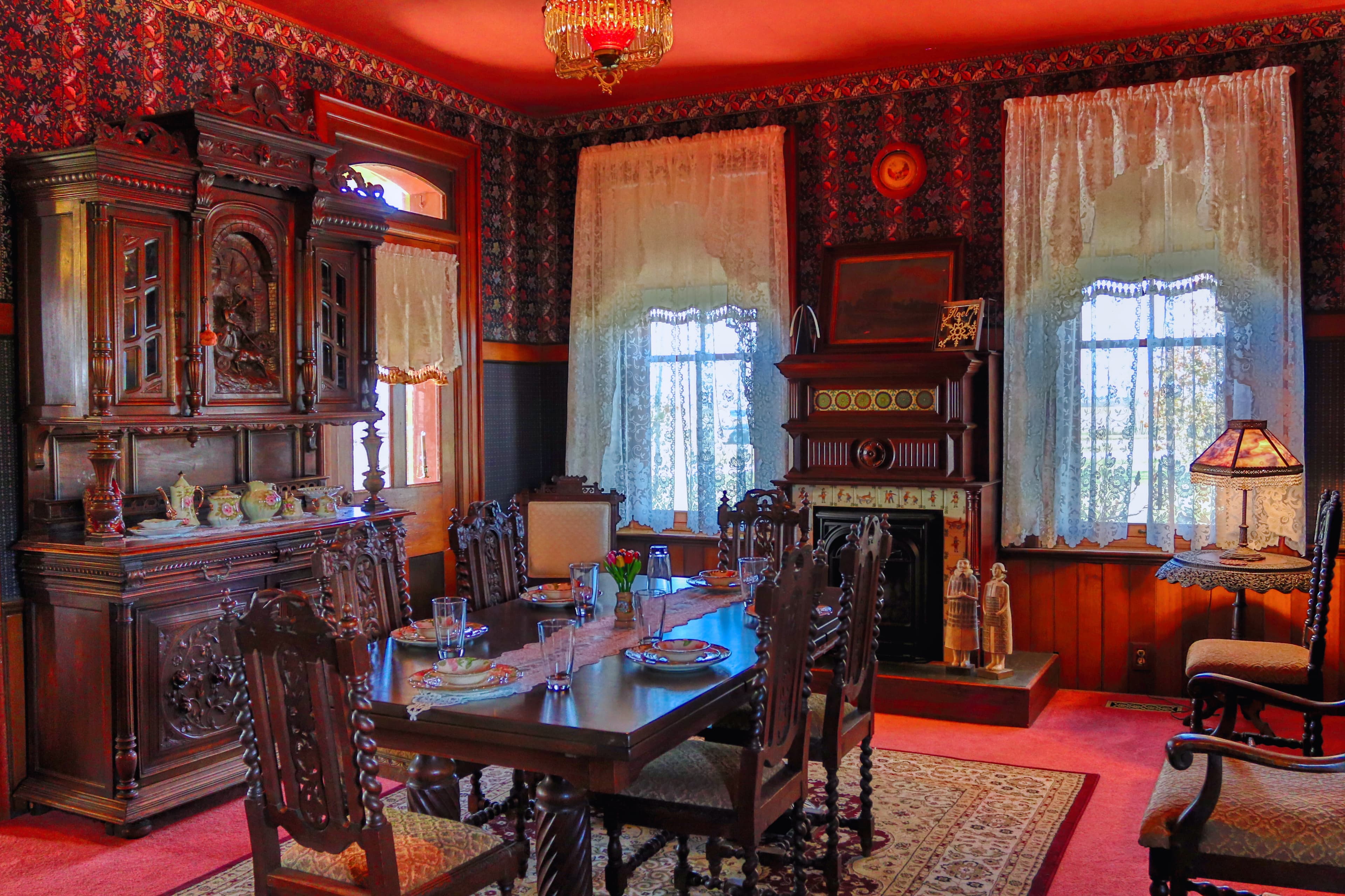 A richly decorated vintage dining room with ornate wooden furniture, lace curtains, and a cozy fireplace.