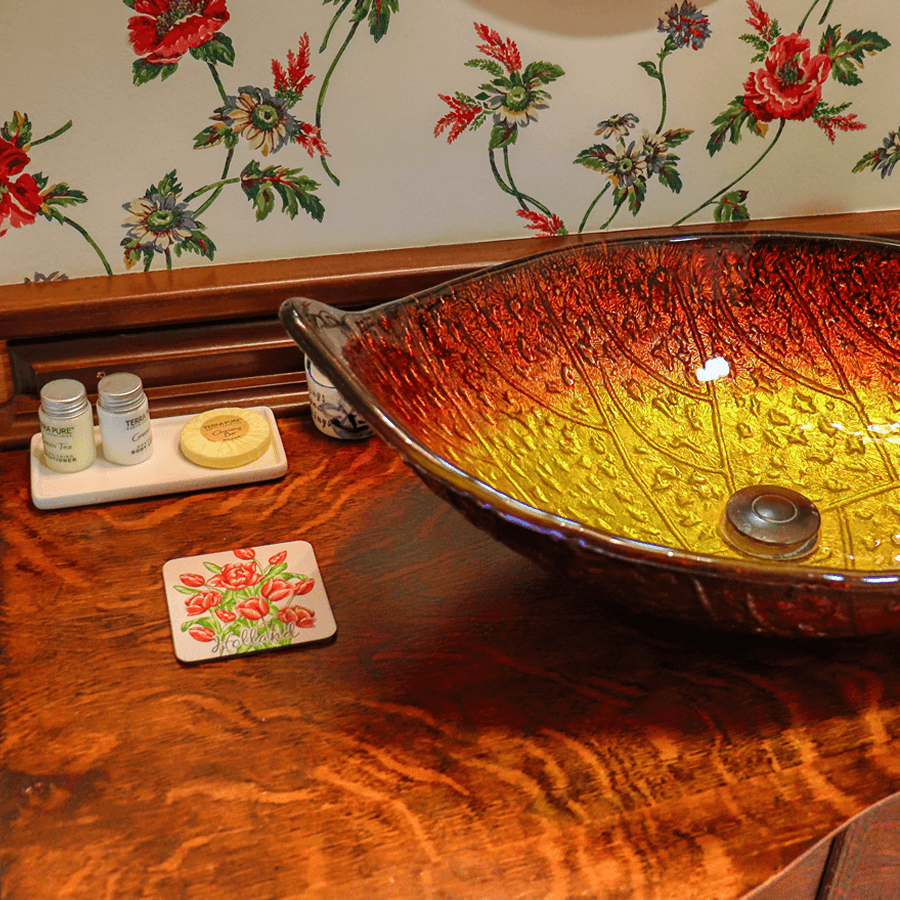 A colorful glass bowl sits on a wooden surface alongside decorative items and floral wallpaper.