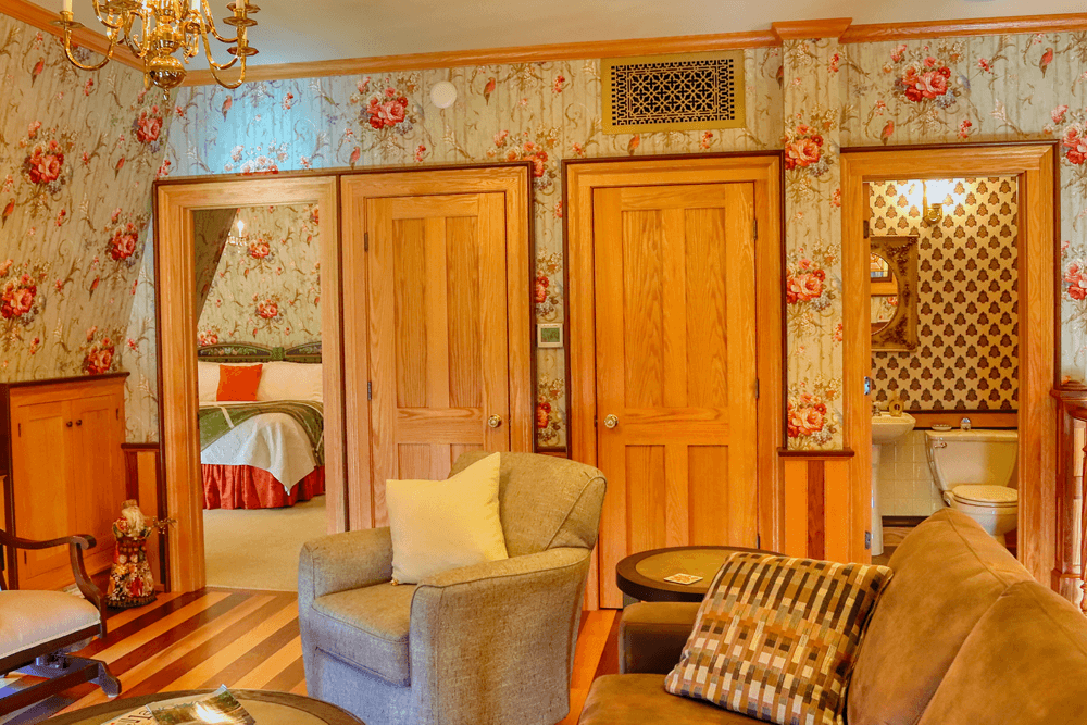 A cozy, vintage-style room featuring floral wallpaper, multiple doors leading to a bedroom and bathroom, and comfortable seating.